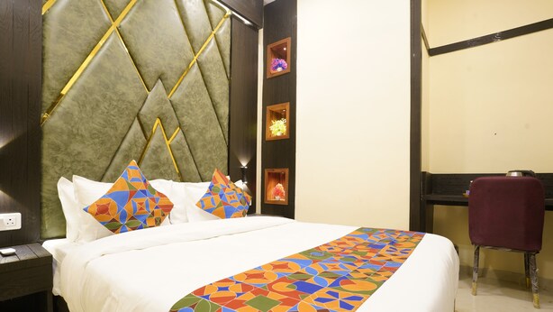 A hotel room with a large bed, a headboard with a geometric pattern, a desk with a chair, and a wall with framed pictures. - Sky Suites By Glitz Hotels (Mumbai)