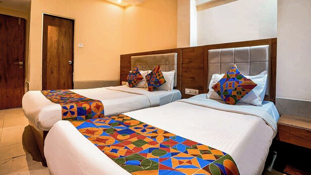 A hotel room with two beds, a wooden door, a ceiling fan, and a window. - Sky Suites By Glitz Hotels (Mumbai)