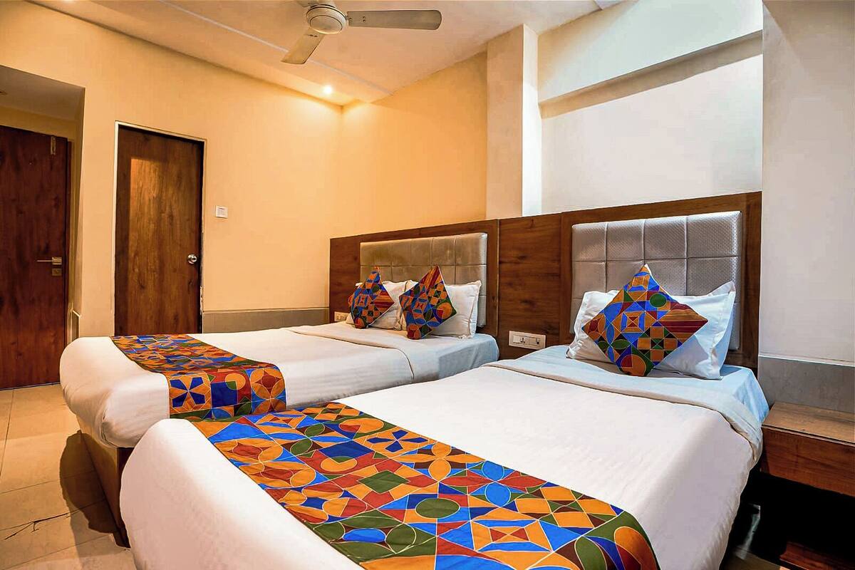 A hotel room with two beds, a wooden door, a ceiling fan, and a window.