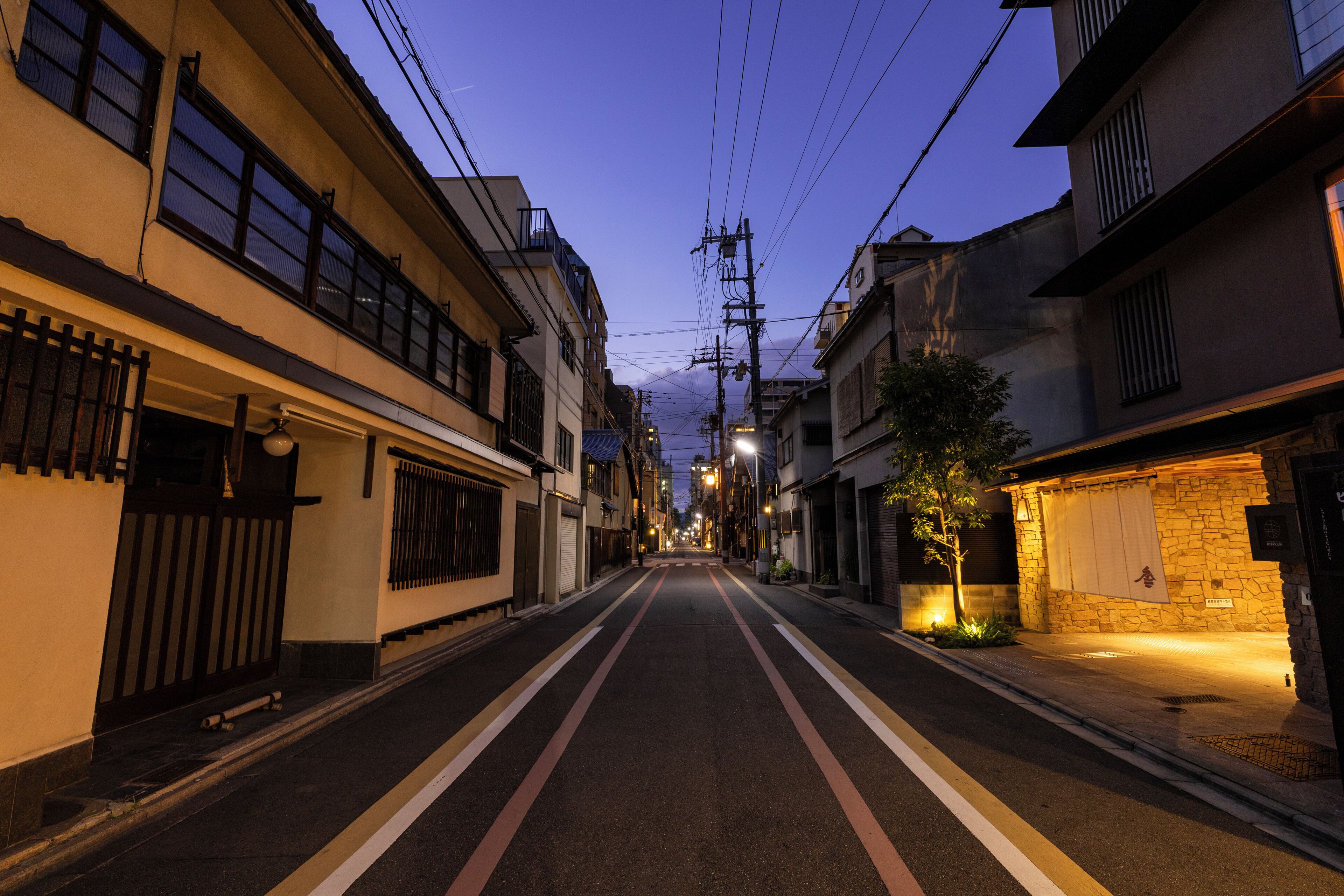 A narrow urban street lined with buildings, some with balconies and others with barred windows.