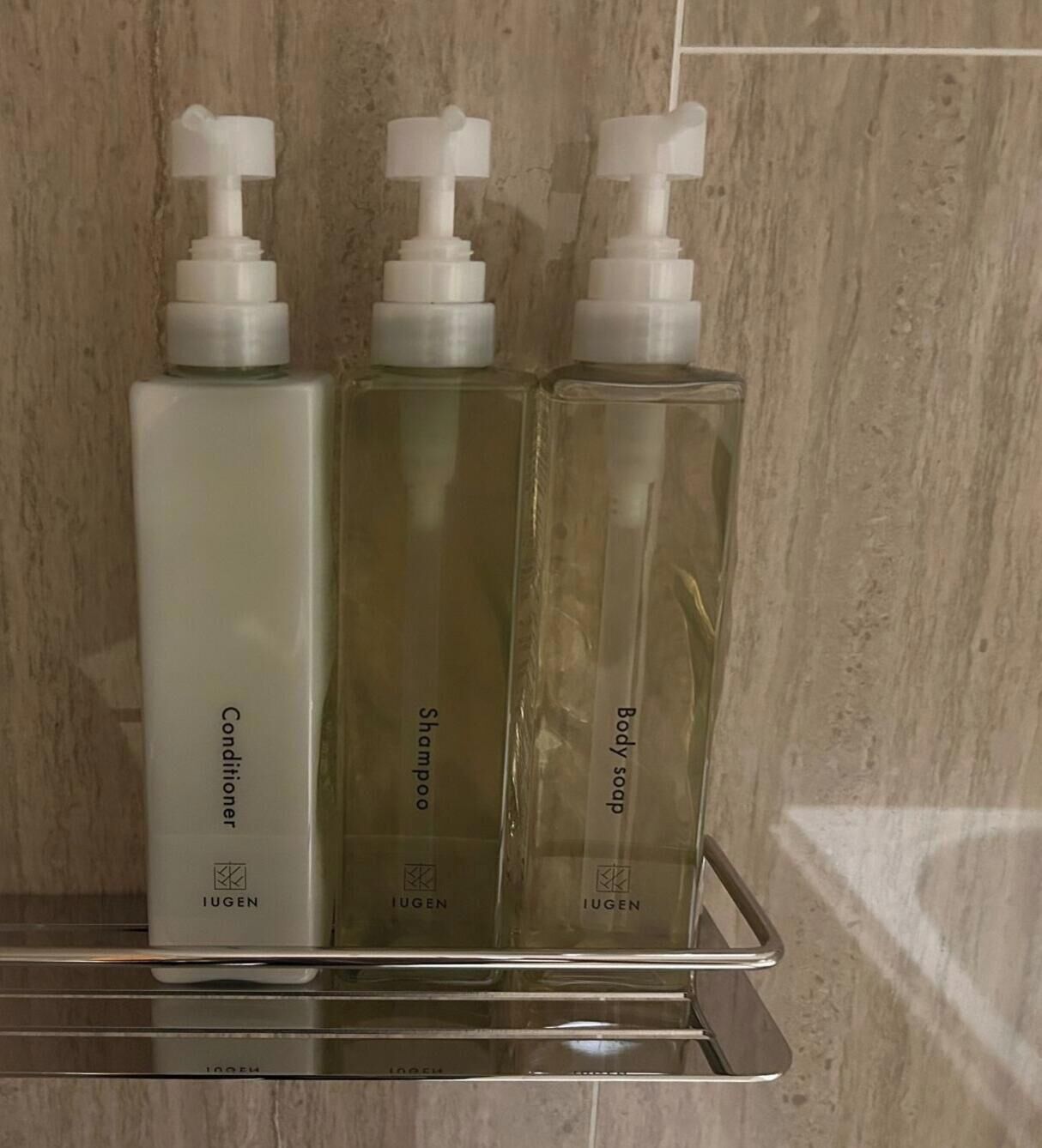 Tres botellas de productos de cuidado personal Iugen sobre una estantería metálica en un baño.