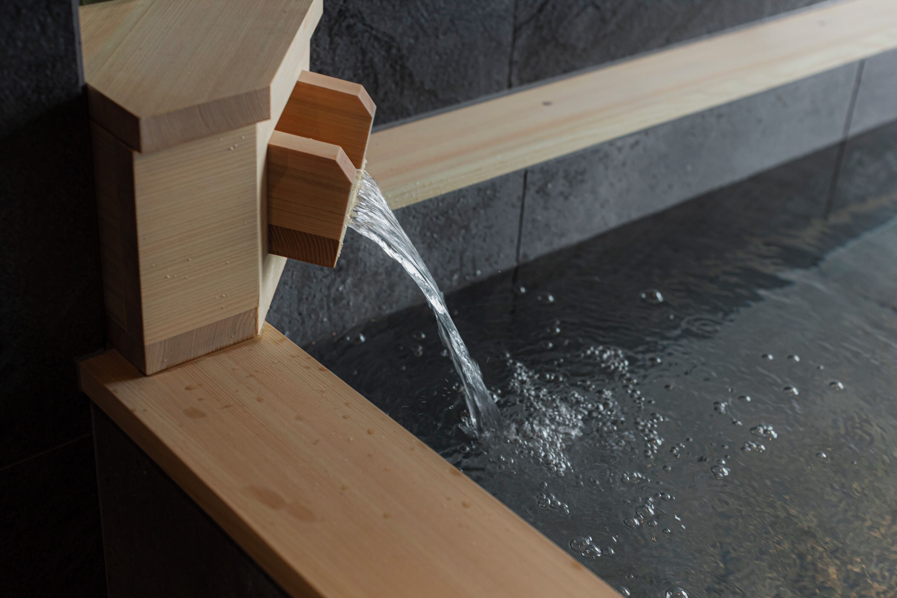 A wooden water feature with water flowing into a stone basin.
