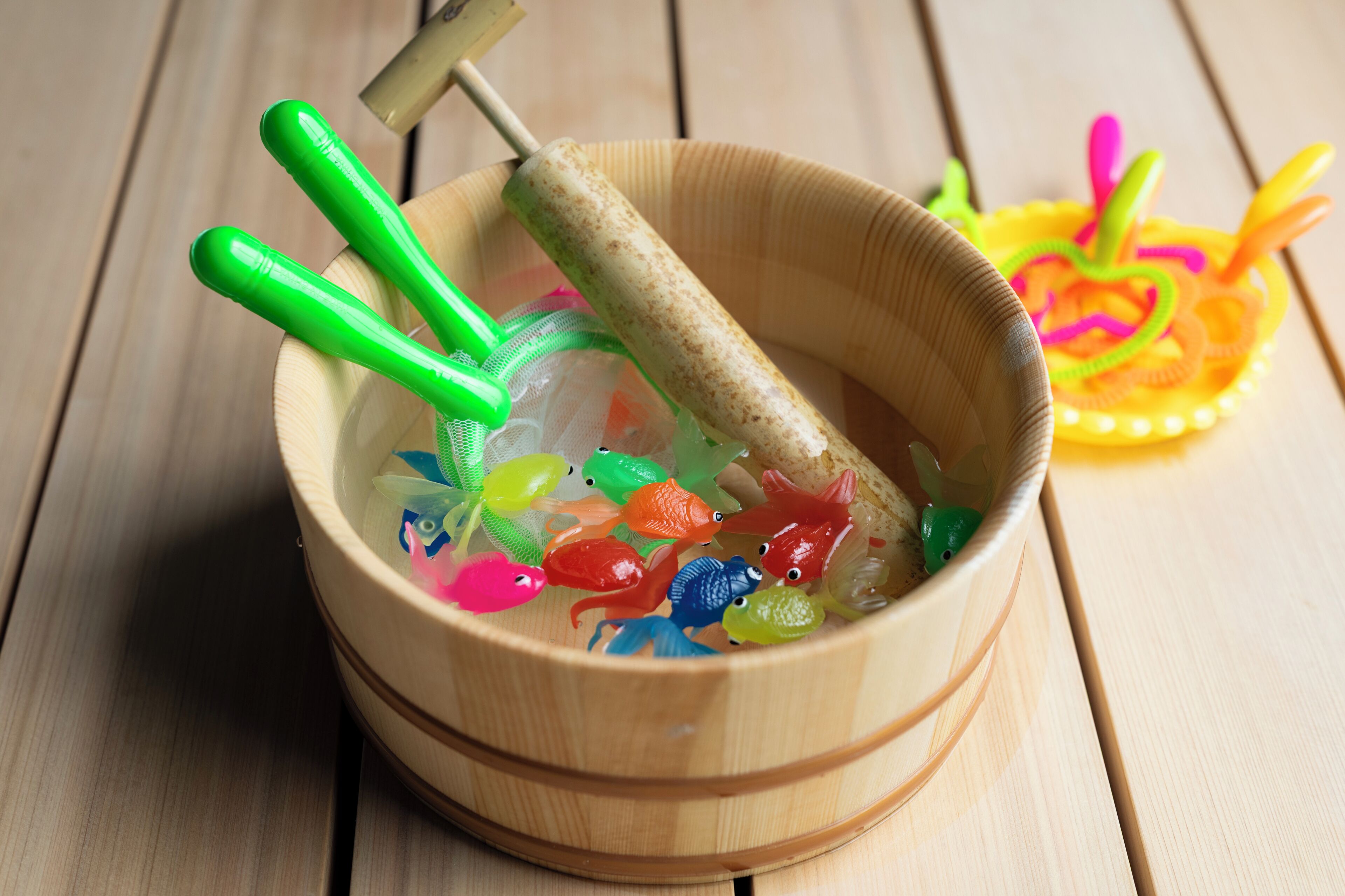 Un bol en bois, avec des poissons en plastique de couleurs vives et un outil à manche vert.
