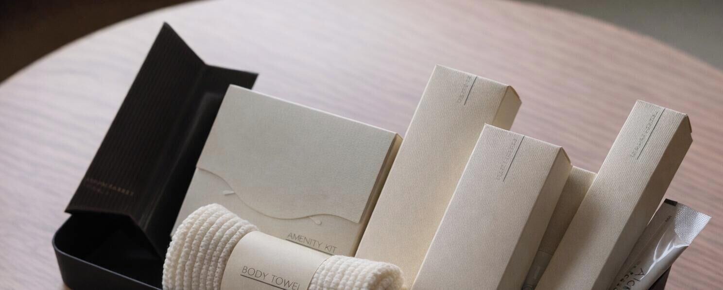 A black box with a white towel and several white towels labeled 'AMENITY KIT' and 'BODY TOWEL' on a wooden surface.