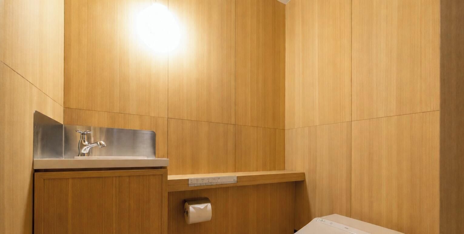 A bathroom with wooden walls, a stainless steel sink, and a toilet paper dispenser.