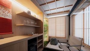 A modern interior with a wooden reception desk, shelves with glassware, a seating area with a rock and white pebbles, and a bamboo plant.