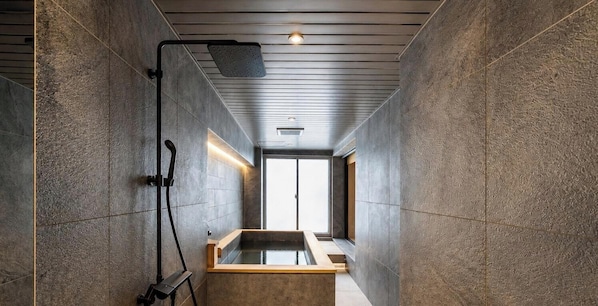A modern bathroom with a large bathtub, a showerhead, and a window providing natural light.