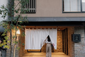 A person standing in front of a building with a stone wall and a wooden floor. - soyo-ka kyoto sanjo (Kyoto)