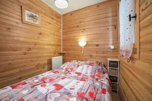A wooden-paneled room with a bed, a wall-mounted light, a radiator, and a small cabinet.