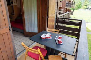 A wooden table with a black tabletop and red chairs, a small wooden bench, and a sliding door leading to a room with a red bed.