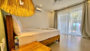 A bedroom with a bed, a wooden bench, a bottle of water, a ceiling fan, and a window with curtains. - Starfish Garden Lodge (Jambiani)
