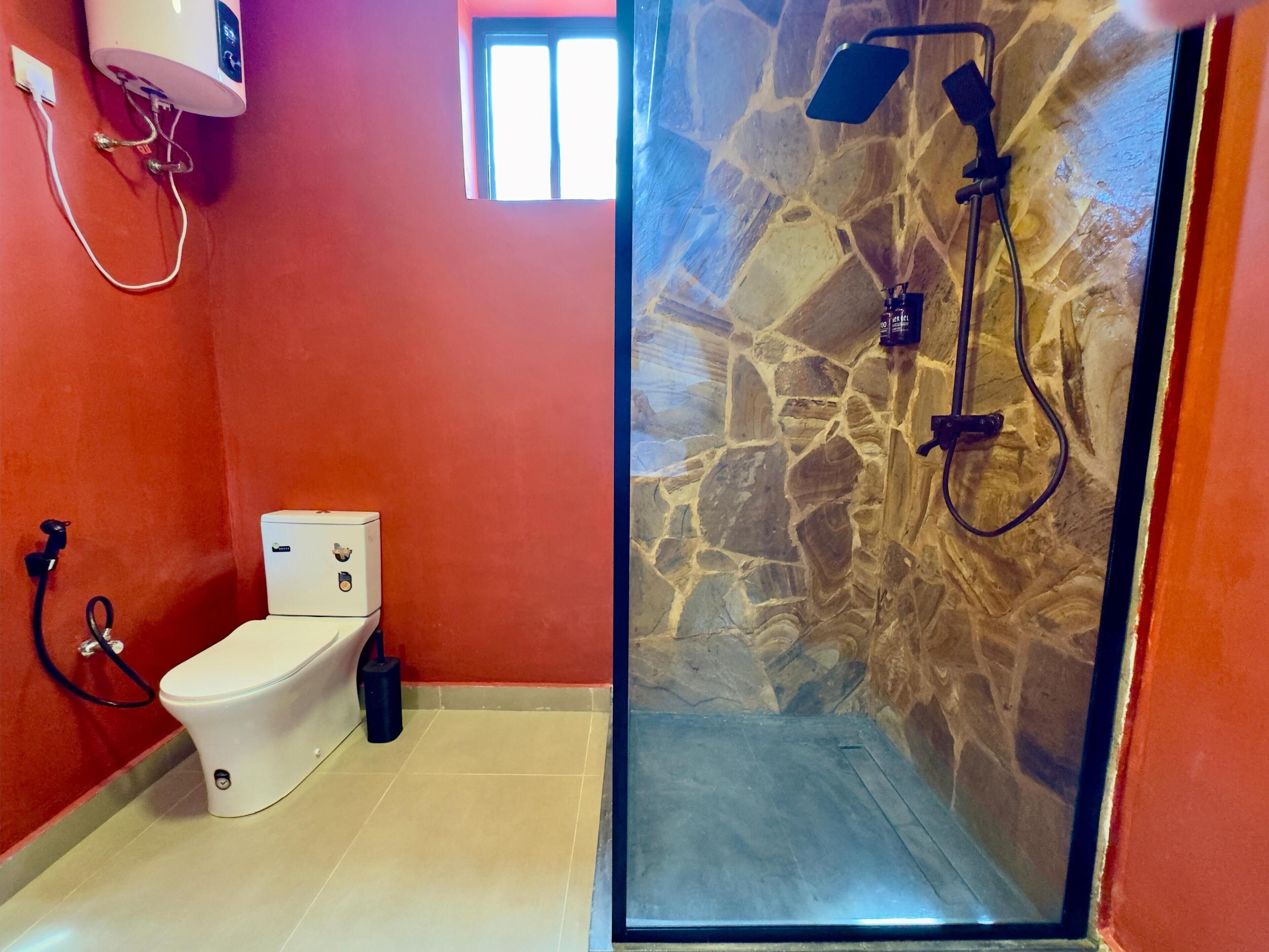 Un baño con inodoro blanco, ducha con pared de piedra y ventana que proporciona luz natural.