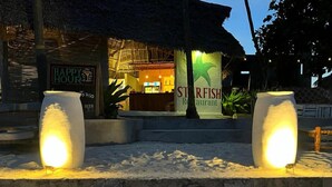 A beachside restaurant named 'ST. RIFISH' with a signboard, two illuminated columns, and a sandy foreground. - Starfish Garden Lodge (Jambiani)