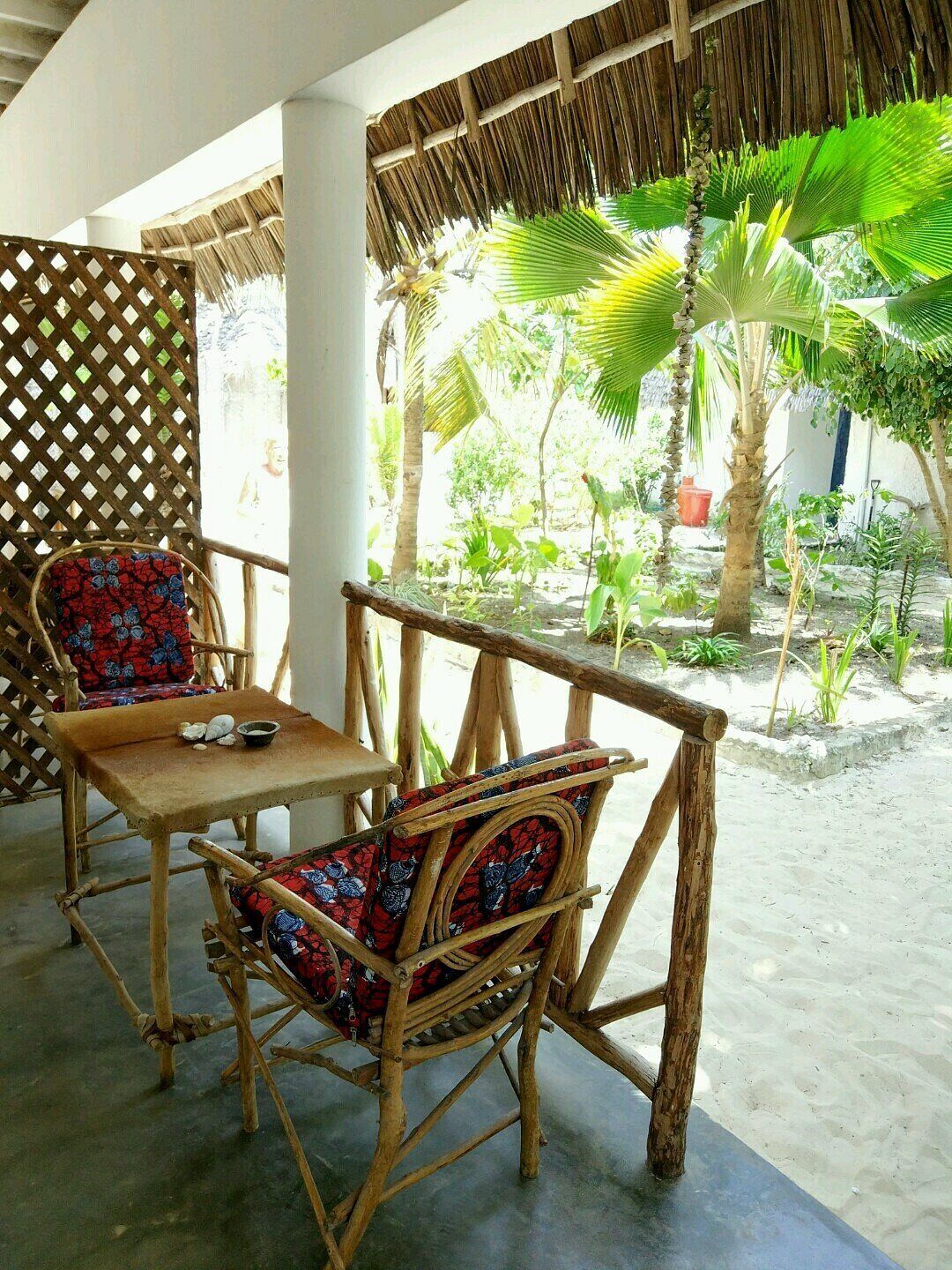 A wooden outdoor seating area with a table and chairs, surrounded by a thatched roof and lush greenery.