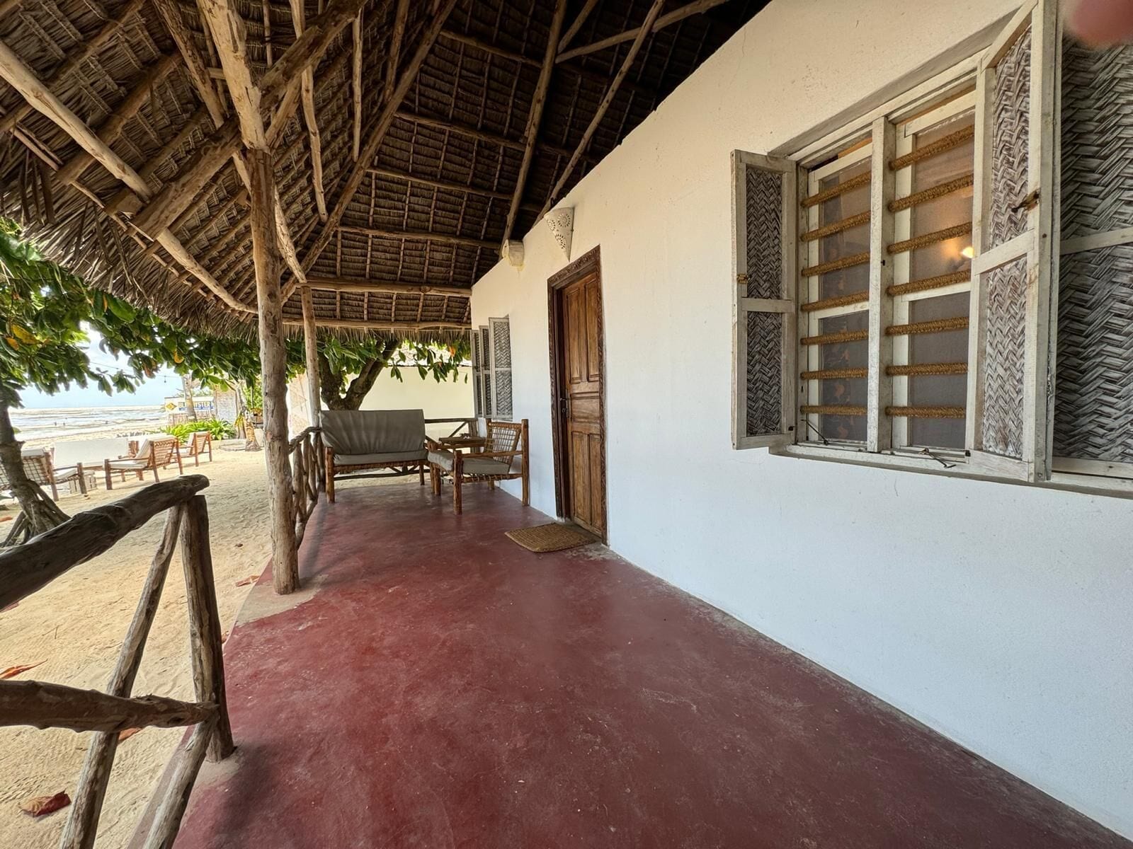 A covered outdoor area with a wooden ceiling, a white wall with a window, and a door.