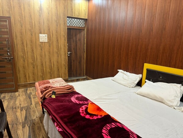 Un dormitorio con un armario de madera, una cama con ropa de cama blanca y una manta roja estampada.