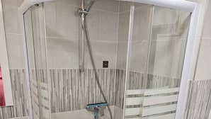 A glass-enclosed shower stall with a handheld showerhead, tiled walls, and a white sink to the left. - Chambre 2 lit simple avec balcon (Lézignan-Corbières)