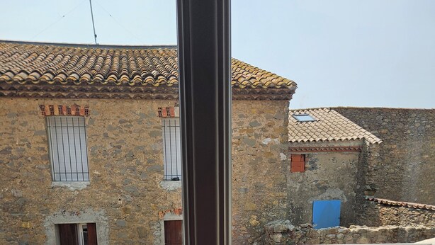 A balcony with a view of a traditional stone building, a table, two chairs, and artificial grass. - Chambre 2 lit simple avec balcon (Lézignan-Corbières)