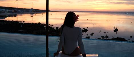 Une personne assise au bord d’une piscine, avec une vue sur le coucher de soleil.