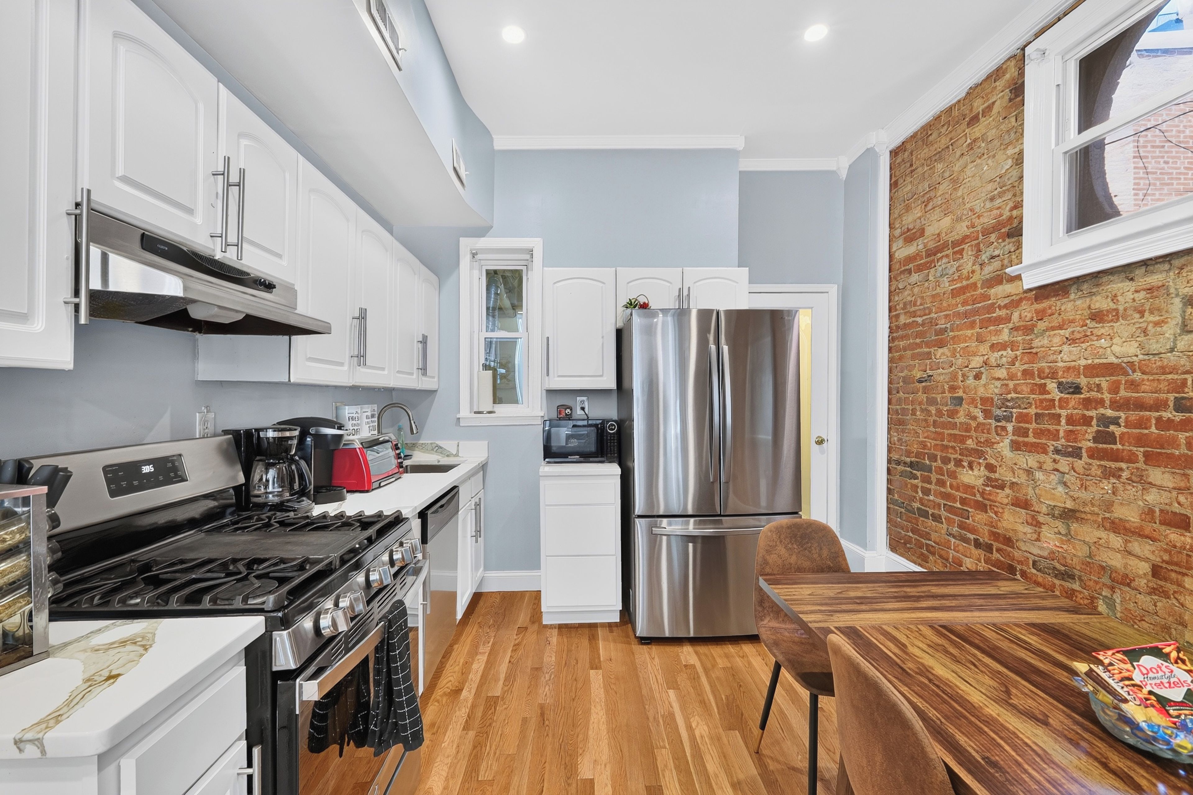 A modern kitchen with white cabinetry, a stainless steel refrigerator, and a wooden dining table.
