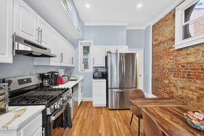 A modern kitchen with white cabinetry, a stainless steel refrigerator, and a wooden dining table.