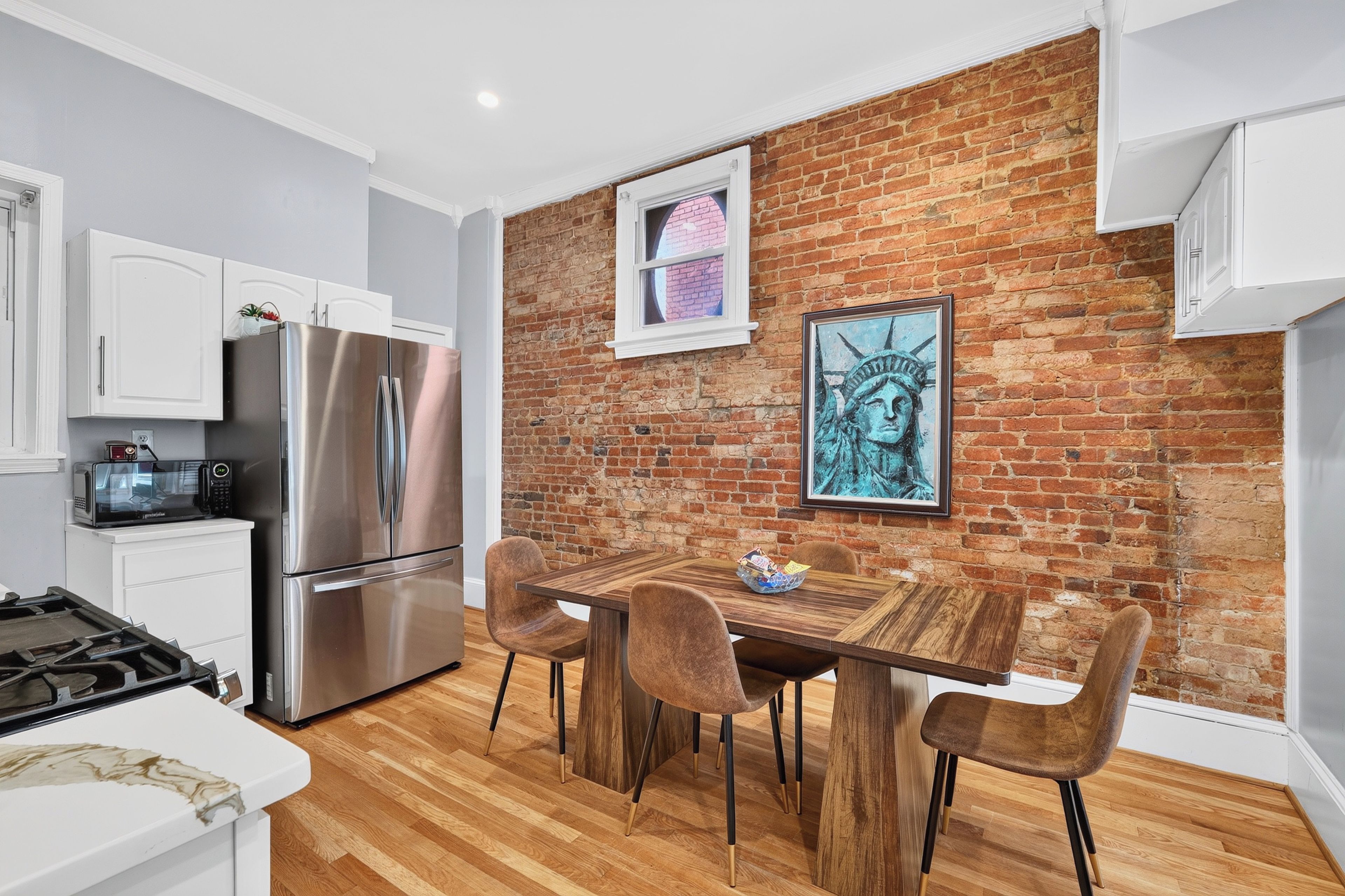 A modern kitchen with a brick wall, stainless steel appliances, and a wooden dining table with chairs.