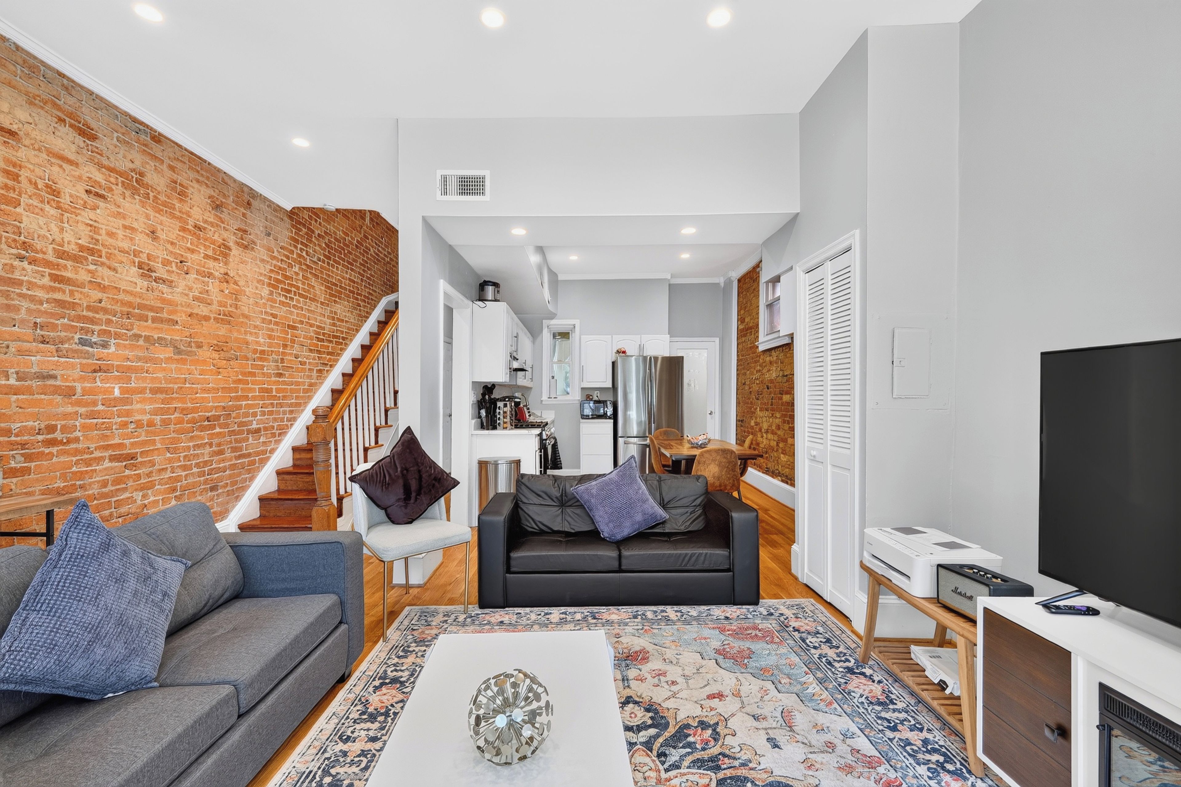 A modern living room with a brick wall, a grey sofa, a black sofa, a coffee table, and a TV on a wooden stand.