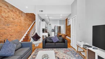 A modern living room with a brick wall, a grey sofa, a black sofa, a coffee table, and a TV on a wooden stand.