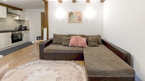A modern living room with a sectional sofa, a small round table, and a kitchen in the background. - Apartment 'Green House' with Private Terrace, Private Garden and Wi-Fi (Neunkirchen)