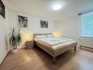 Ein Schlafzimmer mit einem hölzernen Bett, Nachttischen, einer Topfpflanze und zwei gerahmten Kunstwerken an der Wand.