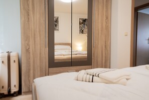 A bedroom with a large mirror, a bed with white linens, a suitcase, and a wooden wardrobe. - Apartment 'Pleißennest' with Wi-Fi (Chemnitz)