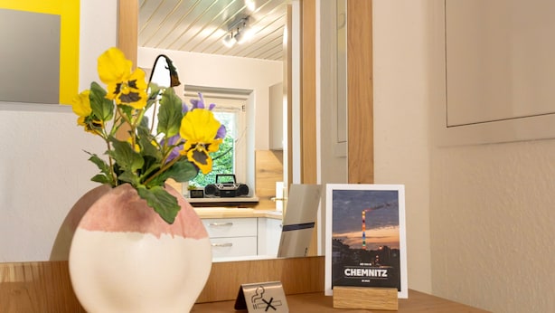 A desk with a vase of flowers, a framed picture, and a small sign. - Apartment 'Pleißennest' with Wi-Fi (Chemnitz)