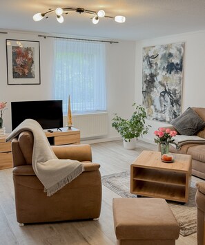 Ein modernes Wohnzimmer mit Sofa, Couchtisch, Fernseher, einer Pflanze und Kunstwerken an den Wänden.