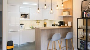 Une cuisine moderne avec des meubles blancs, un four à micro-ondes encastré, une machine à café et un coin bar équipé de deux tabourets.