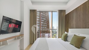 A modern hotel room with a large bed, a mounted TV displaying 'NETFLIX', and a view of a cityscape through large windows. - Torani by Kozystay - TB Simatupang (Jakarta)