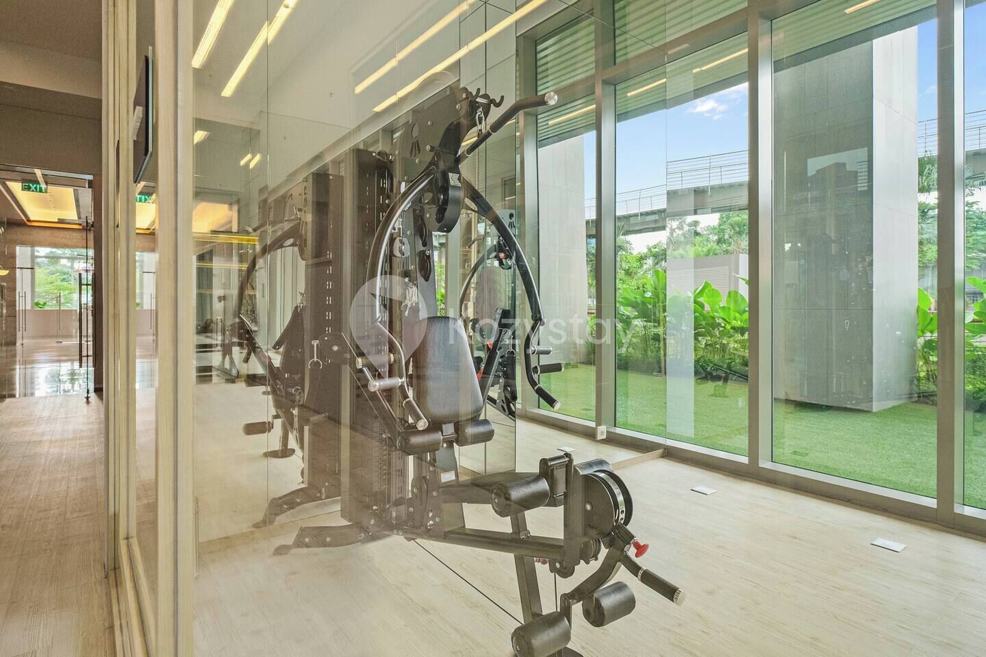 Een sportschool met trainingsapparatuur, grote ramen en uitzicht op groen.