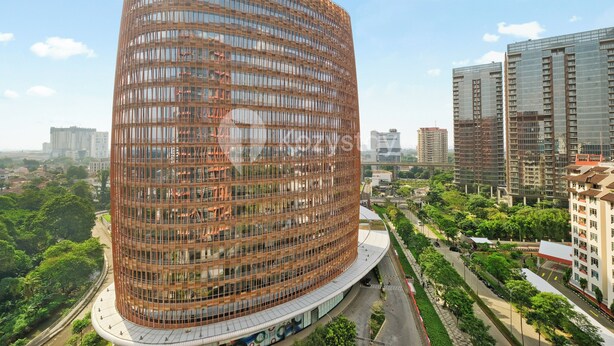 A modern, curved building with a grid-like facade, surrounded by greenery and other high-rise buildings. - Torani by Kozystay - TB Simatupang (Jakarta)
