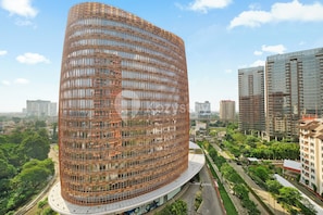 Un bâtiment moderne à la forme incurvée, doté d’une façade en forme de grille, entouré de verdure et d’autres immeubles de grande hauteur.