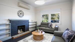 A living room with a fireplace, a sofa, a coffee table, and a window with a view of the outside.