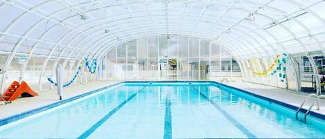 Une piscine intérieure dotée d’un toit en verre, d’une eau cristalline et de quelques éléments de décoration colorés.
