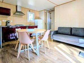 A modern kitchen with wooden cabinets, a dining table with chairs, and a grey sofa in a living area.
