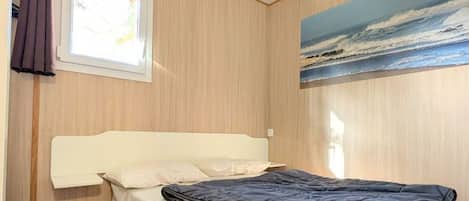 Une chambre à coucher avec un lit, une fenêtre et un tableau représentant une scène de plage.
