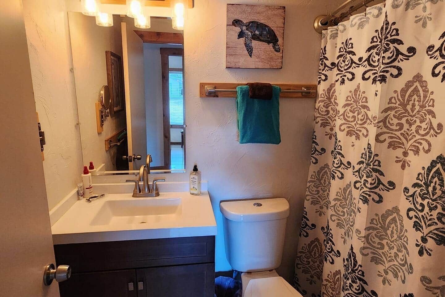 Une salle de bain équipée d’un lavabo, d’un miroir, de toilettes et d’un rideau de douche.