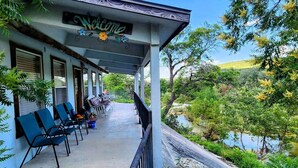 A covered porch with a 'Welcome' sign, outdoor seating, and a view of a river and greenery.