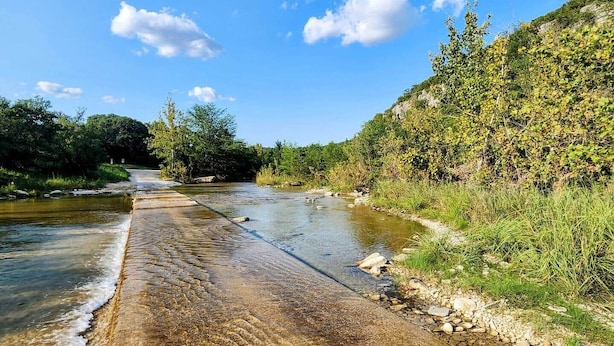 A river with a concrete path alongside it, surrounded by greenery and trees.