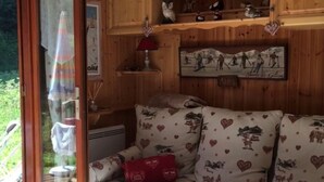 Habitació acollidora amb interior de fusta, un sofà amb coixins de cor, una taula petita amb una làmpada i una estant amb objectes decoratius.