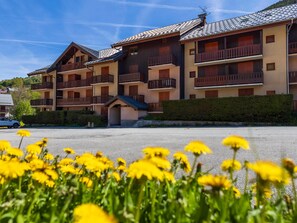 Ein mehrstöckiges Hotel mit Balkonen, einem Parkplatz und gelben Blumen im Vordergrund.