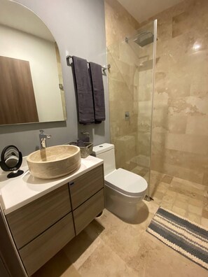Une salle de bain avec un lavabo rond, des toilettes et une douche à parois de verre.