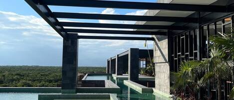 A modern outdoor pool area with a checkered floor, a covered seating area, and a view of a lush landscape.