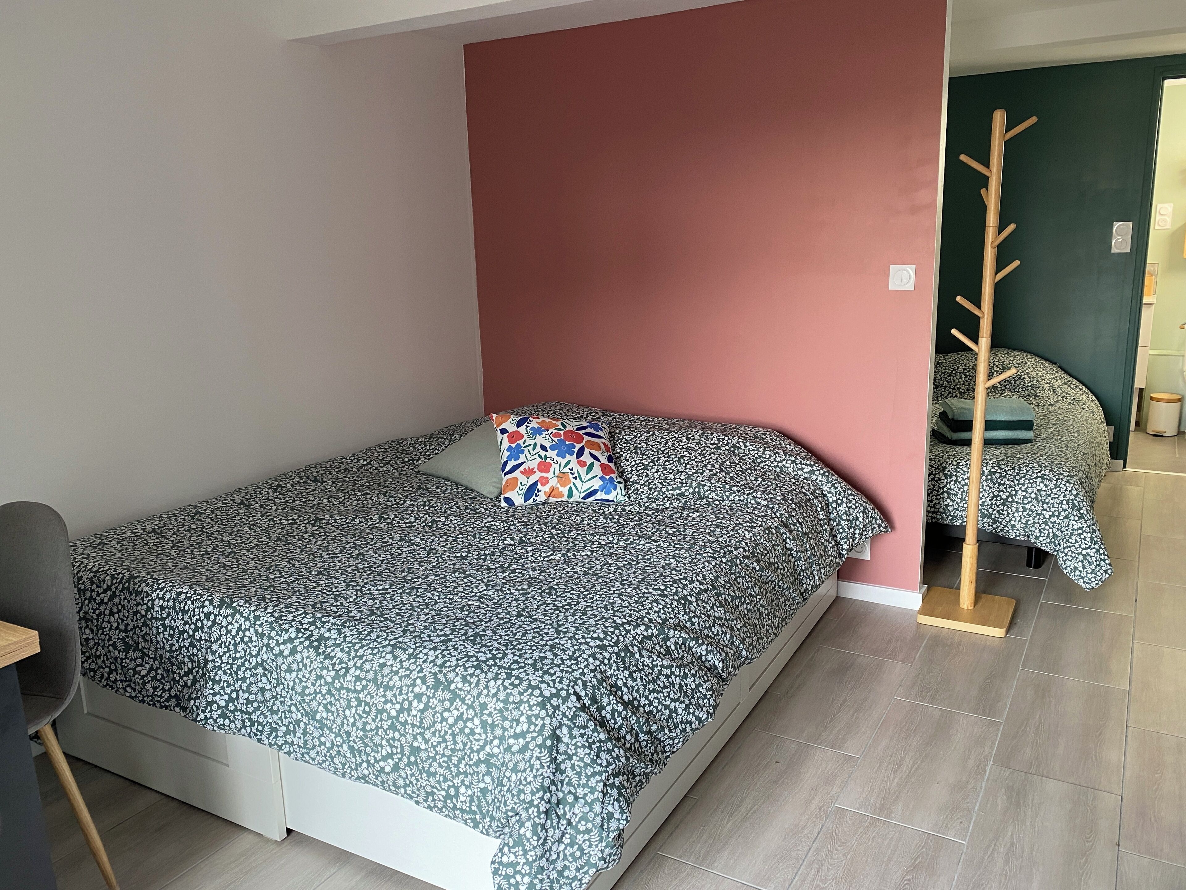 Un lit simple avec une couvre-lit à motifs floraux, un mur d’accent rouge et un porte-manteau en bois.